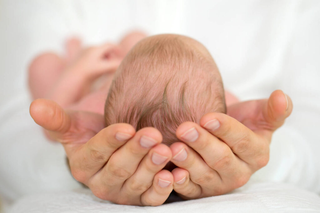 Men’s Hands holding newborn baby.